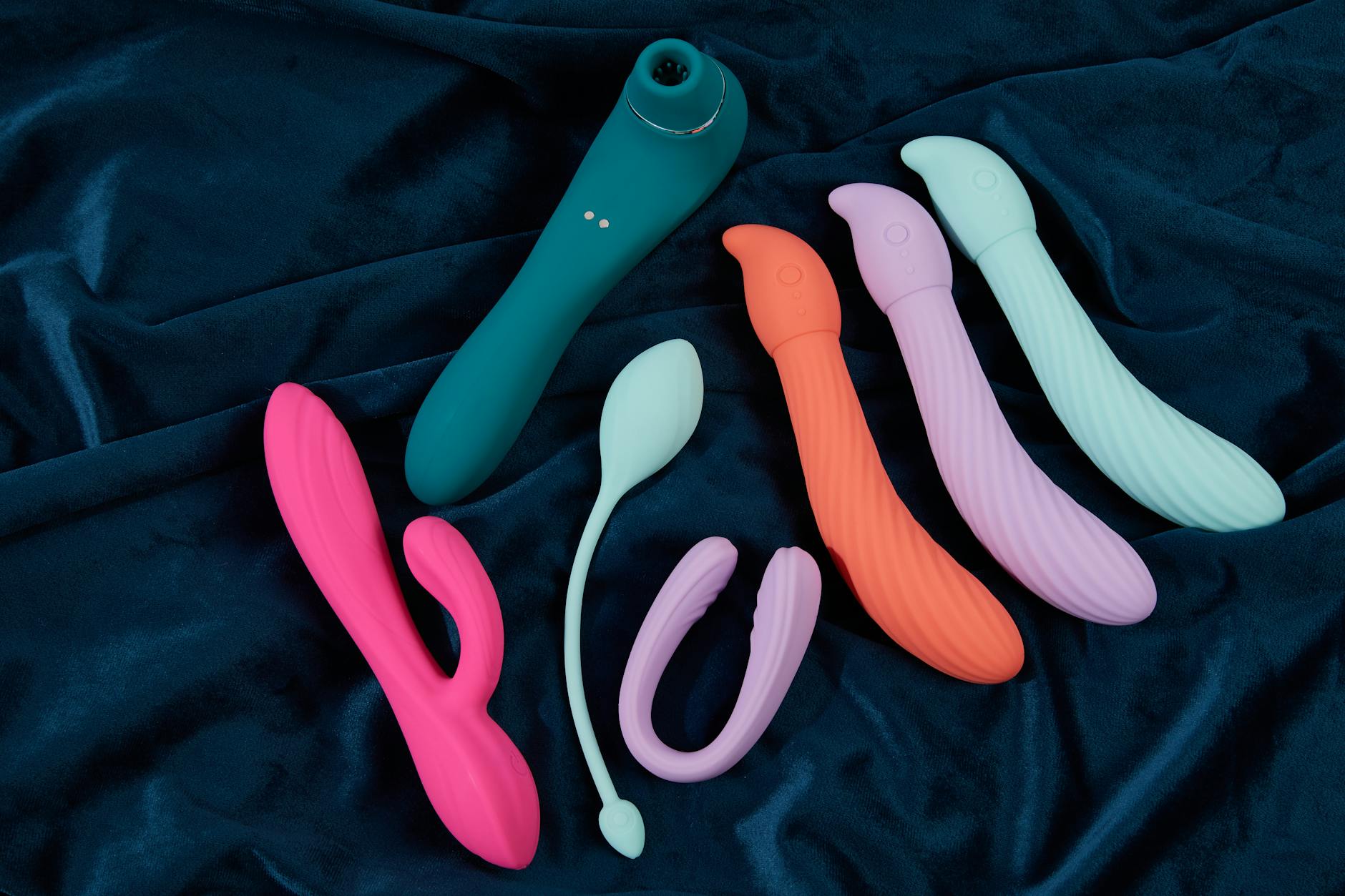 Vibrant display of silicone clitoral vibrators on dark fabric, showcasing various shapes designed for pleasure at every age