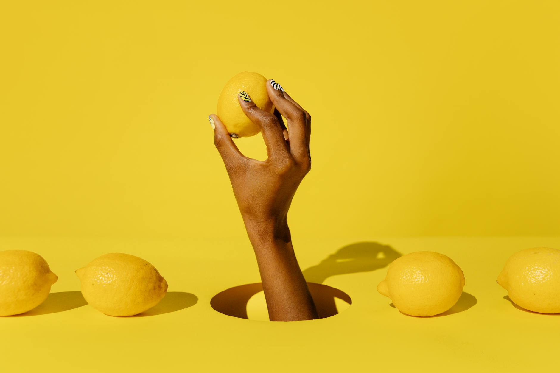 Hand holding a fresh lemon against a vibrant yellow background, symbolizing natural pleasure and sensuality