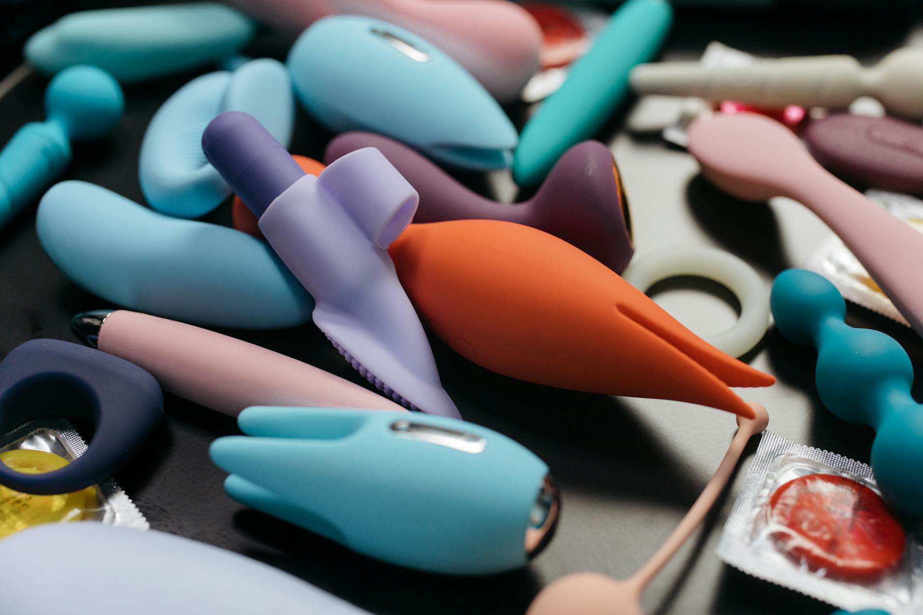 Two hands holding pink and blue silicone vibrators against a pastel background.