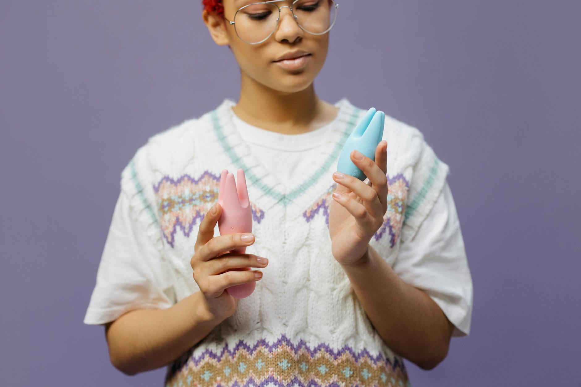 Woman thoughtfully holding a blue and pink vibrator, exploring pleasure and connection.