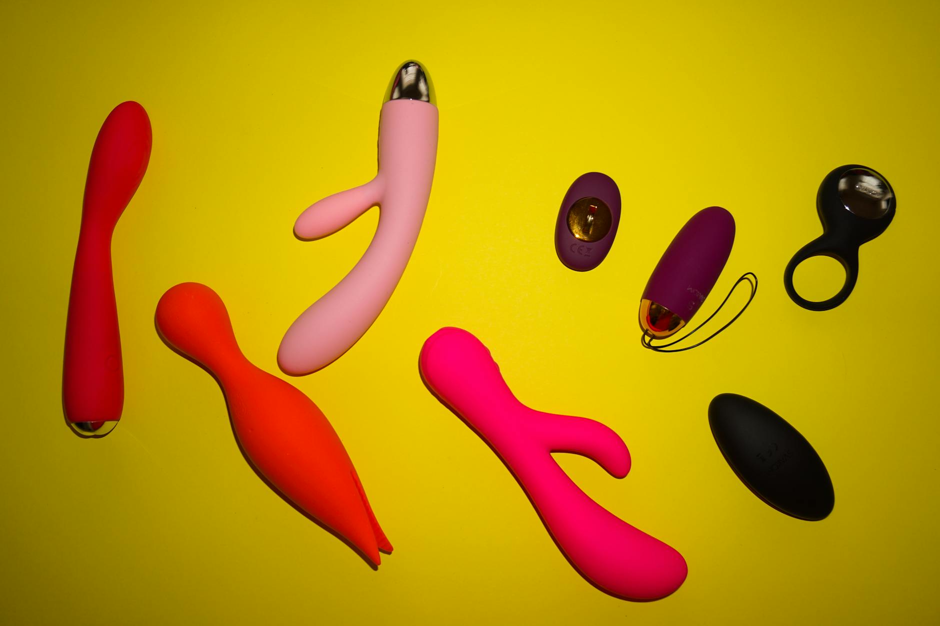 Collection of colorful vibrators and adult toys displayed on a bright yellow background
